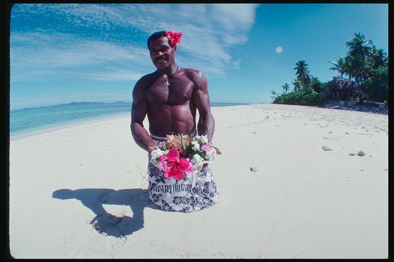 Мужчина с венком с розовых и белых цветов на белом песке пляжа