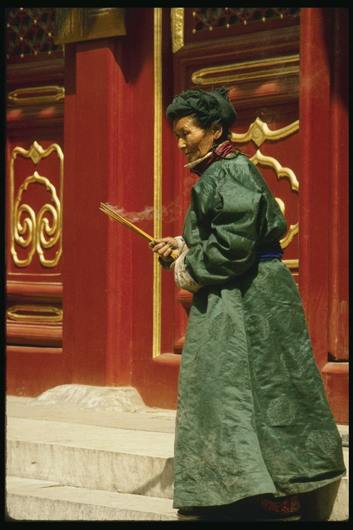 Женшина с дымящими ароматными палочками возле стен храма