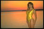 Девушка в золотистом купальнике на фоне заходящего солнца