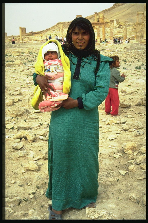 Женщина с младенцем на руках на фоне руин города