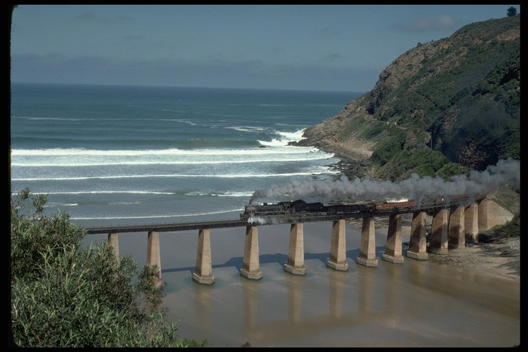 Мост через реку впадающую в море, по котором проезжает задымленный поезд
