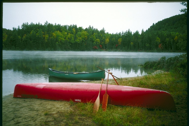 På bredden af floden er en rød kano med årer. Green kano i vandet nær kysten