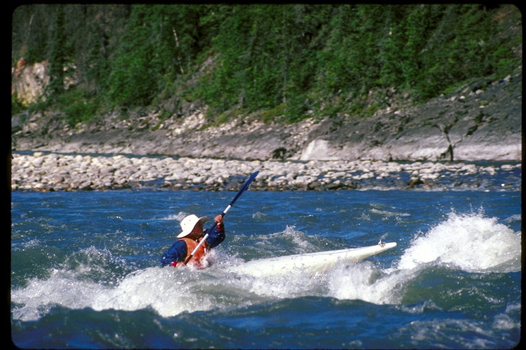 Человек плывёт на белом каяке  по реке среди гор