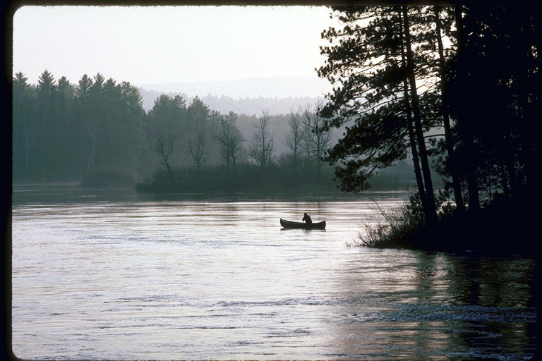 Чёрно - белая фотография лесного озера. Рыбак на лодке на середине озера  ловит удочкой рыбу