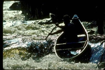 Atlet - extremals dalam perahu kayu merambat melalui jeram sungai berbatu gunung