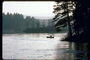 Чёрно - белая фотография лесного озера. Рыбак на лодке на середине озера  ловит удочкой рыбу