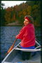 Девушка в красном свитере, плывущая на байдарке осенним днём