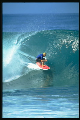 На красной доске по синей воде прорезает волны серфингист