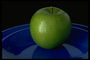 Зеленое яблоко в керамической тарелке темно-синего цвета